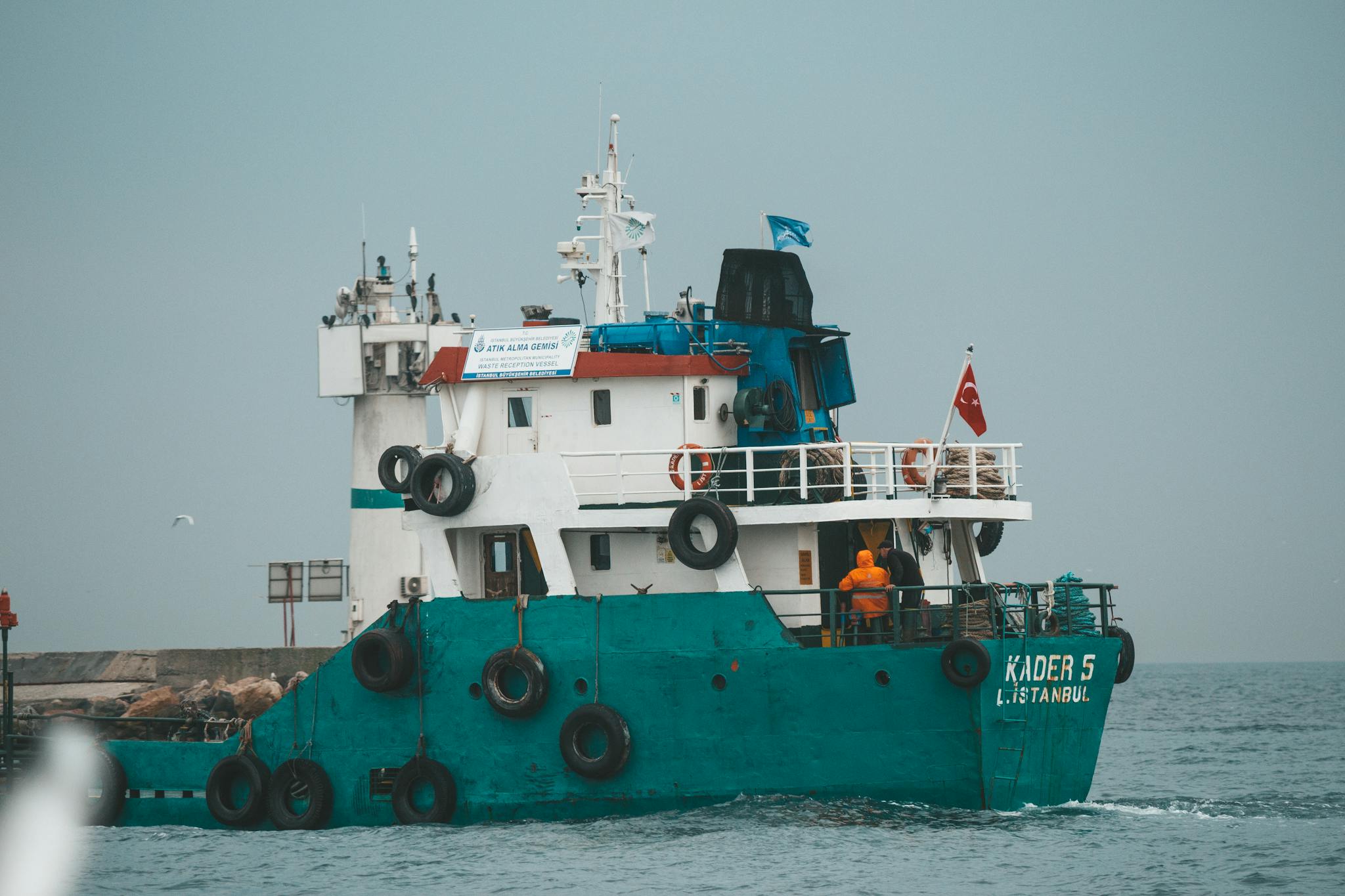 Photo by Emre Can Acer Unrecognizable people on deck of green and white vessel floating on rippling sea against gray sky